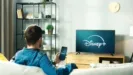 Man watching television in his living room, the television showcases the Disney+ start screen
