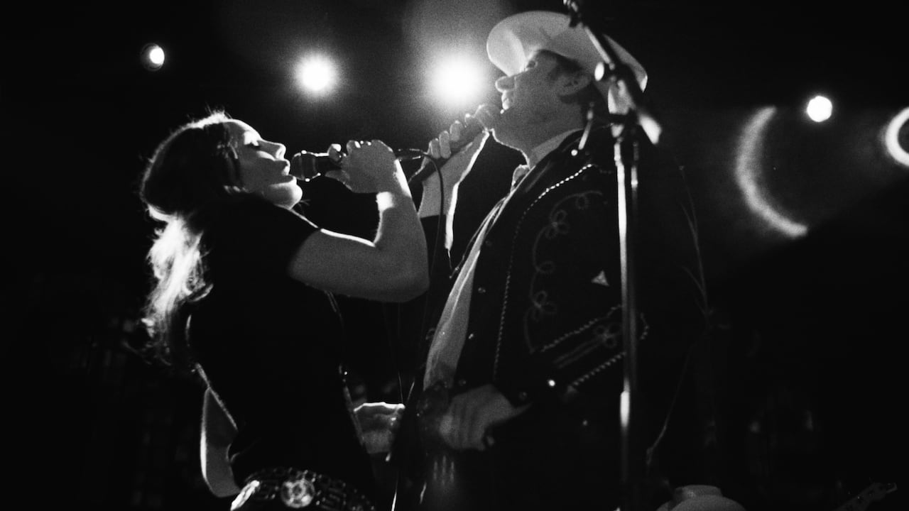 A man and a woman stand onstage holding microphones and singing.