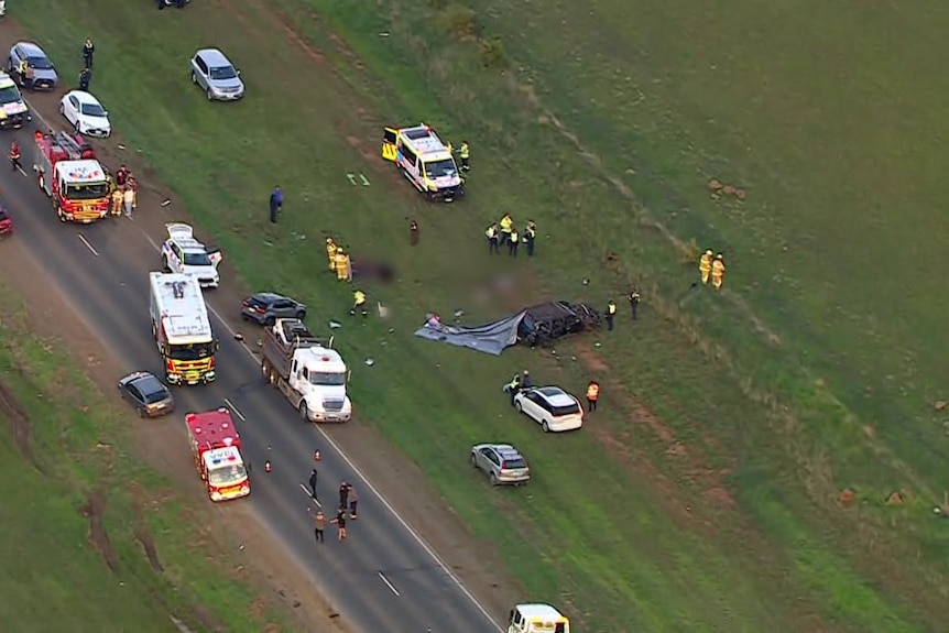 An aerial shot of a crumpled car beside a roadway covered in ambulances and fire engines and a helicopter.