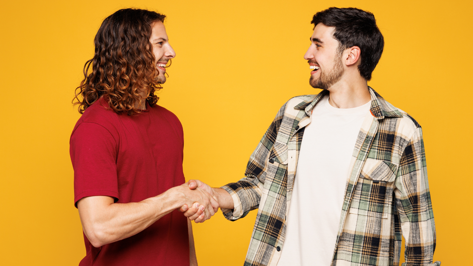 two casually dressed young men shaking hands and smiling