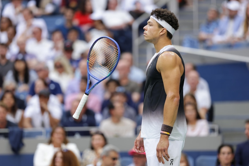 Ben Shelton's tennis racquet hovers in front of him as the crowd watches in the background
