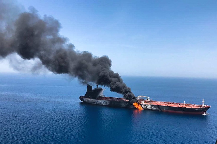An oil tanker at sea is on fire with a large cloud of smoke coming out of it