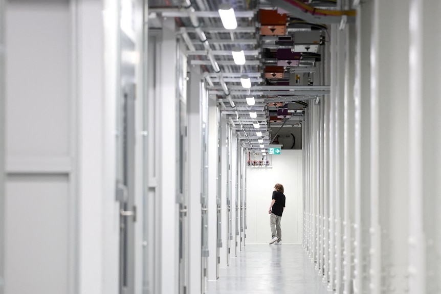 a person walks between rows of white data centre cabinets.
