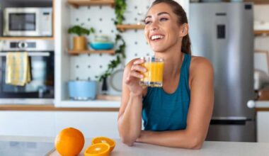 Beautiful young woman drinking fresh orange juice in kitchen.