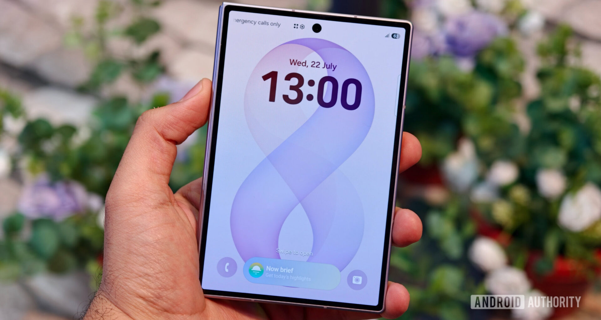A hand holding the closed Samsung Galaxy Z Fold 8 showing its outer cover display with a digital clock and wallpaper