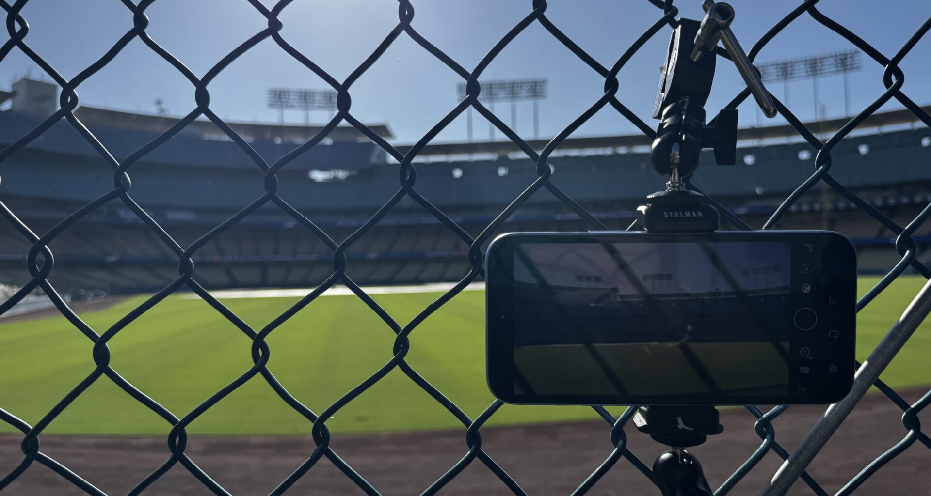 A phone mounted to a tripod behind a fence looking from the bullpen onto the field.