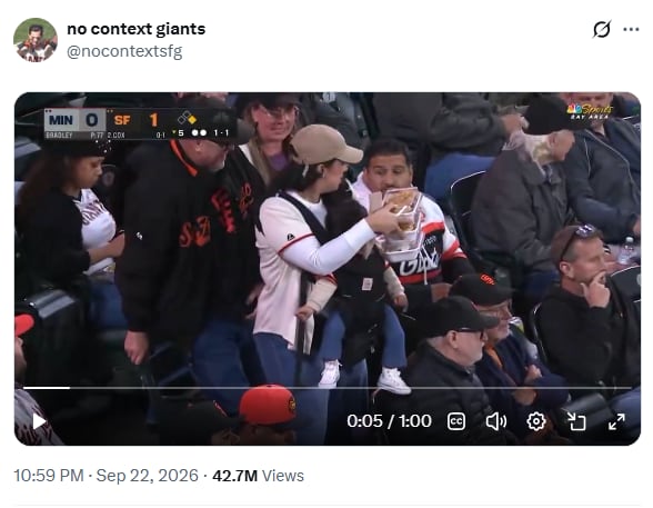 An image showing a woman with a baby strapped to her front edging into a stadium seat holding three trays of food.