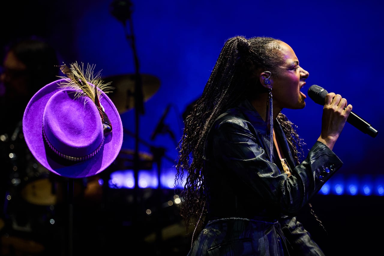 A woman sings into a microphone on stage in front of a purple hat