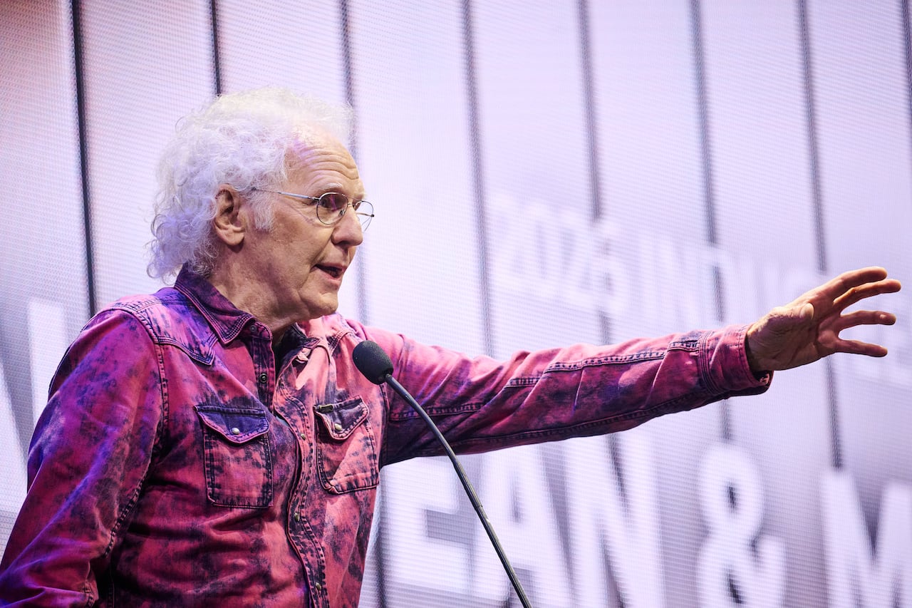 A man reaches out his arm as he speaks into a microphone