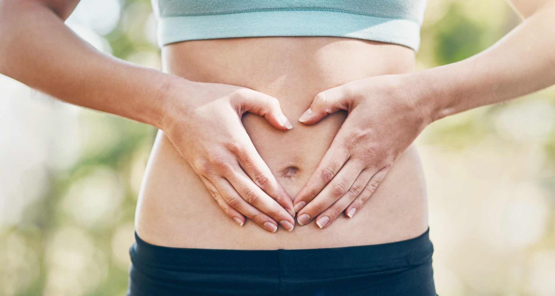 Abdomen of woman in sports gear. Hands are across stomach in the shape of a heart for gut health
