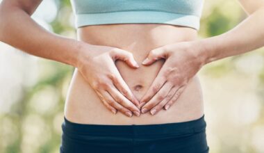 Abdomen of woman in sports gear. Hands are across stomach in the shape of a heart for gut health