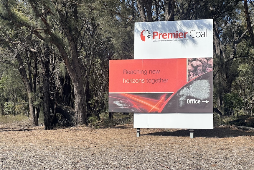 A sign that says "Premier Coal" stands near some trees in a country area.