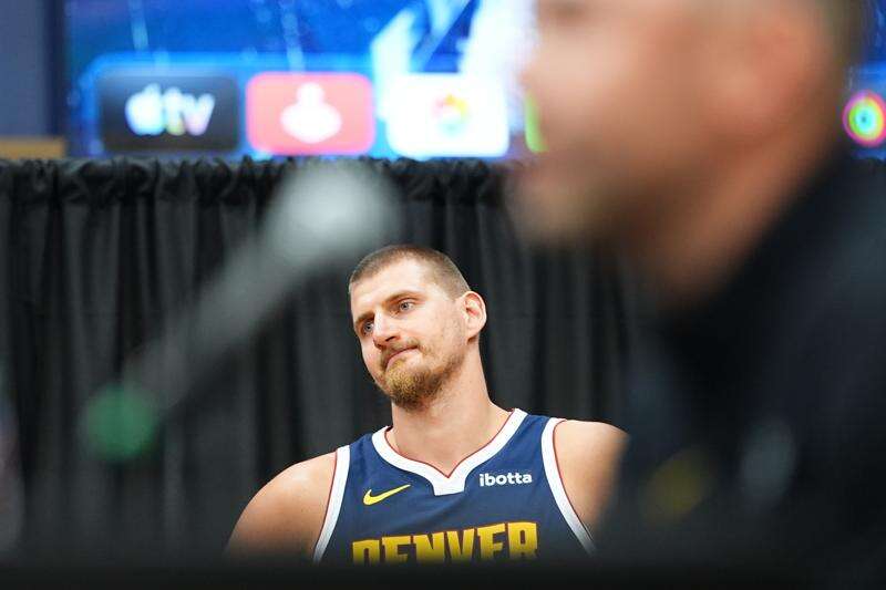 Denver Nuggets center Nikola Jokić, back, is framed between the microphone and head coach David Adelman as he responds to questions during the NBA basketball team's media day Monday, Sept. 28, 2026, in Denver. (AP Photo/David Zalubowski)
