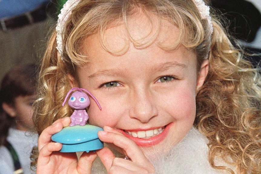 A young girl holds a purple toy close to her face.