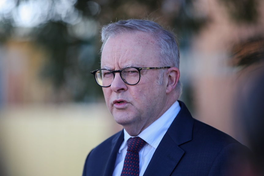 the prime minister in a suit and glasses addresses a press conference
