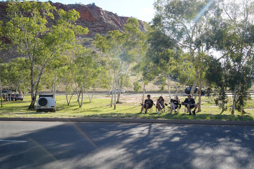 Group of young people sit on camping chairs next to road in front of escarpment 