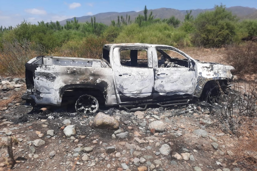 A large white ute sits in grassland, covered in burn marks.