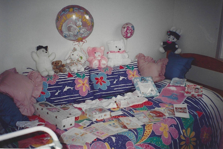 A bed with stuffed bears, balloons and baby clothes on top.