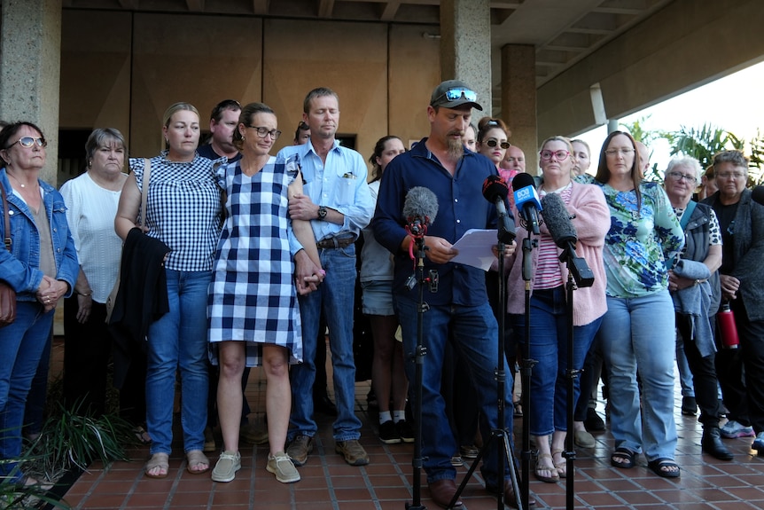 A large group of people outside of a court house standing around a microphone.