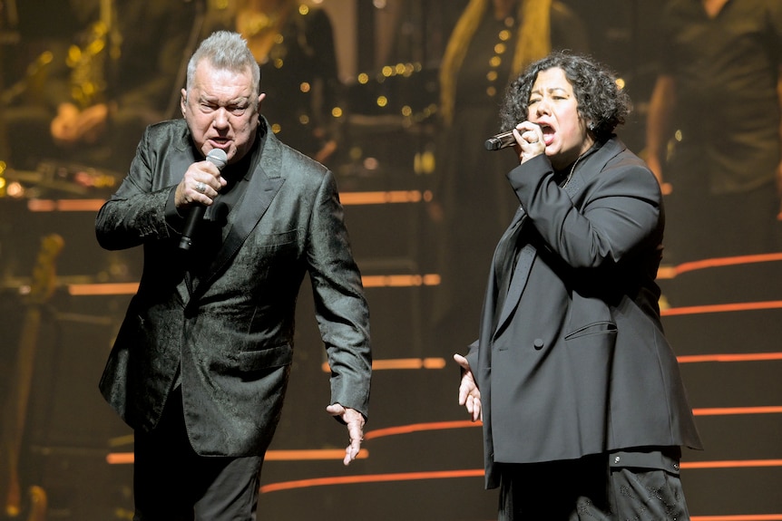 Jimmy and Mahalia Barnes, wearing black, sing into microphones.