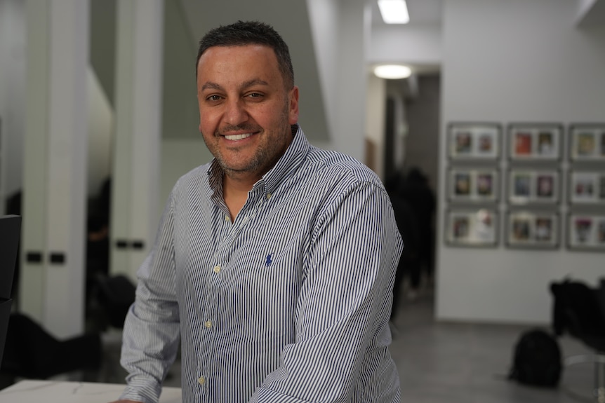 a middle-aged man smiling wearing a striped collared shirt in a hair salon