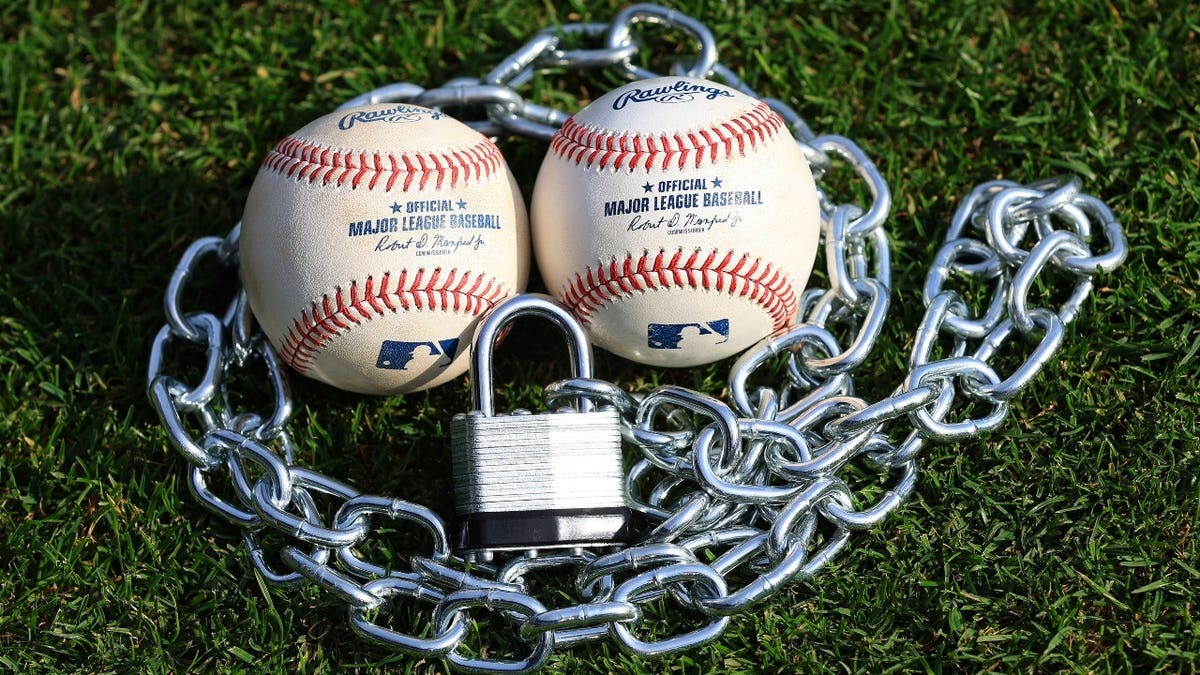 A locked padlock and chain against two official MLB baseballs representing a potential lockout between MLB and the Major League Baseball Players Association (MLBPA) for the 2027 season.