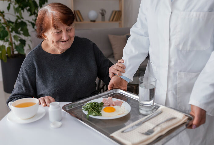 A healthcare professional serving an elderly woman a meal, highlighting routine medical procedures doctors do.