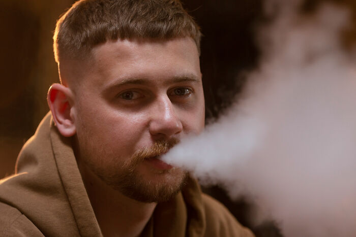 A man exhales vapor from a vape, a habit patients often lie about to doctors during medical exams.