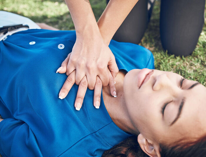 Hands performing CPR on a person lying on the grass, illustrating critical medical procedures doctors do.