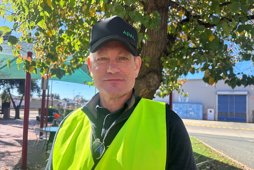 A man in a cap and high visibility vest stands in a factory courtyard