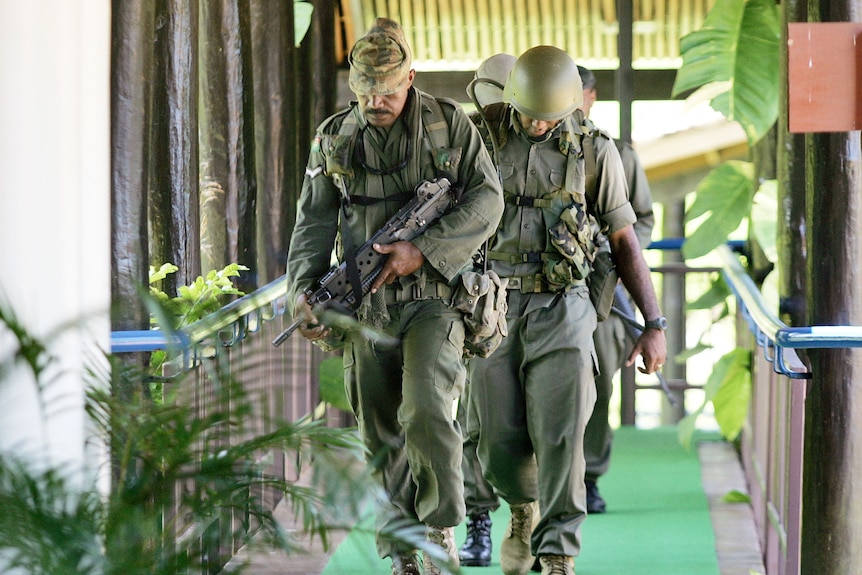 Fijian soldiers in full uniform with heads down.
