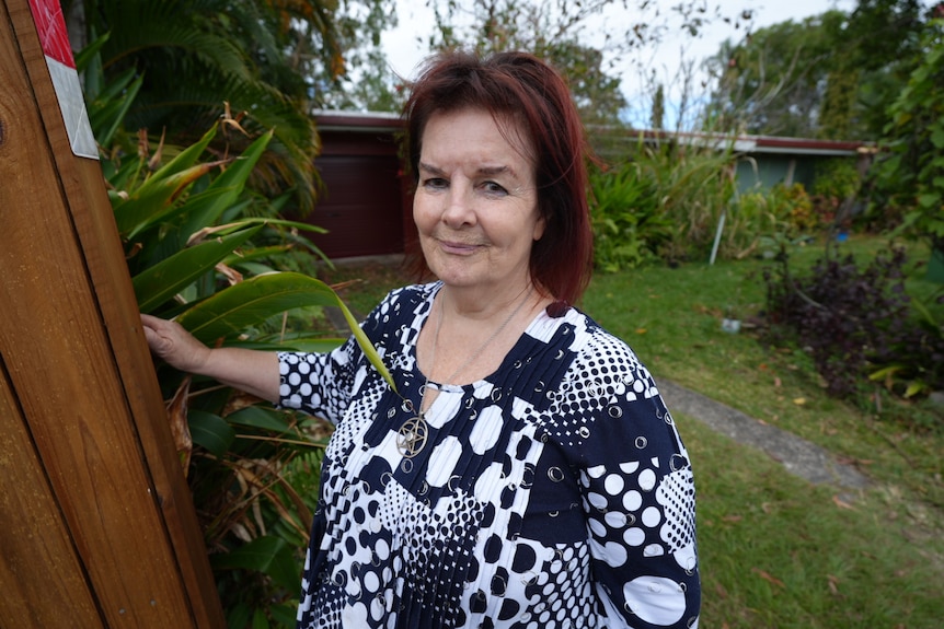 A portrait of a woman standing next to a fence in front of a home.