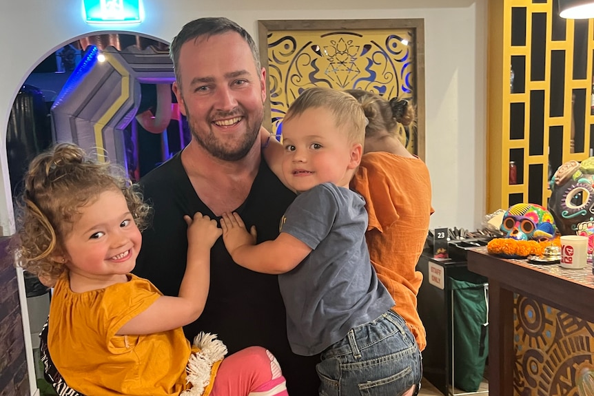 A man smiling holding two toddlers.