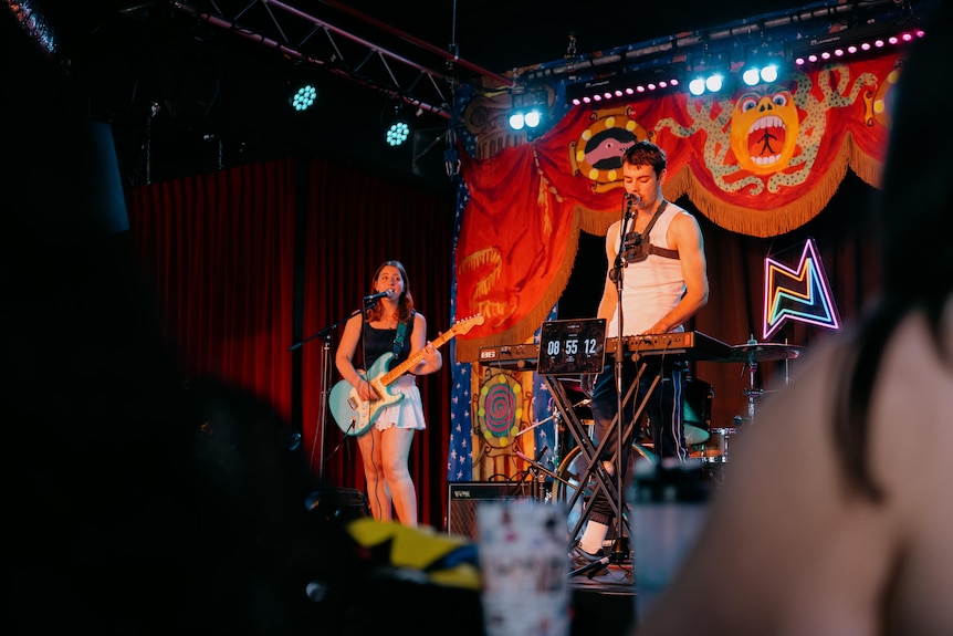 a young man and woman play music on a stage in a music venue