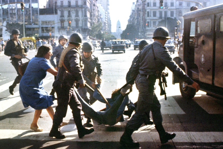 Military officers in Argentina carry a man towards a truck, while a woman tries sto stop them.
