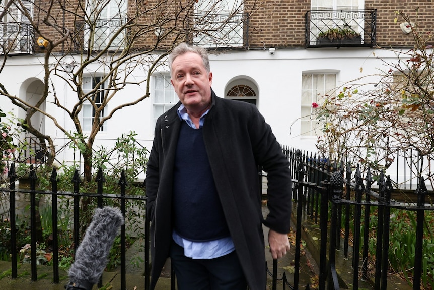 A man walking through a gate, and looking at the camera with a neutral expression.