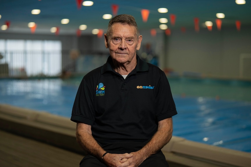 Greg Hodge looks at the camera sitting on a seat in front of his indoor swimming pool school