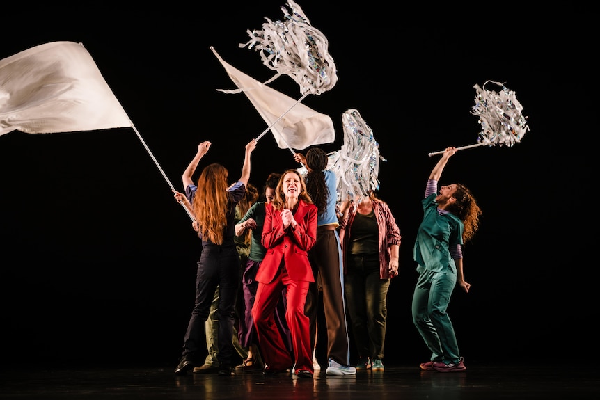 Performers waving flags on stage against a pitch-black background.