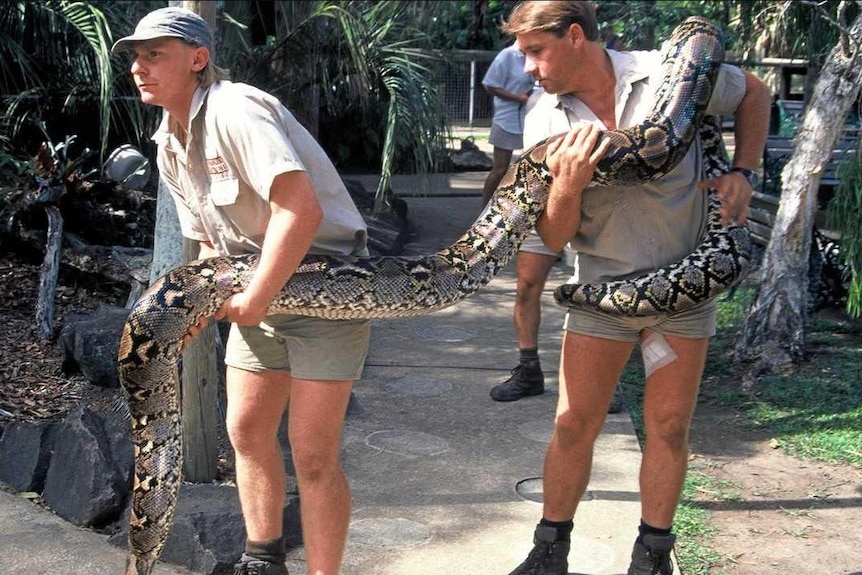 Two men holding a massive snake while outside