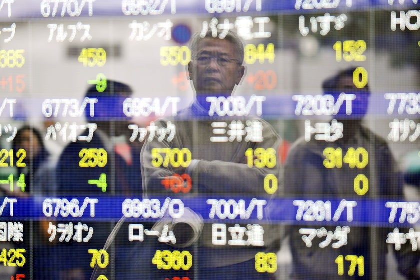 The stock market, a screen with rows of numbers and faces of Japanese men and women standing and watching it.