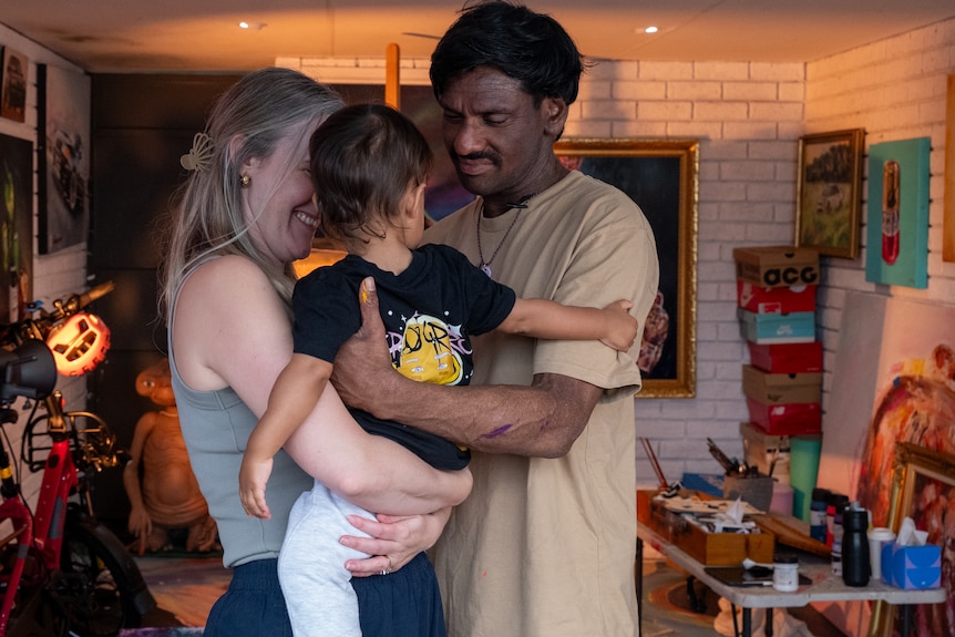 A man and a woman hold a baby while hugging each other in an artist's studio