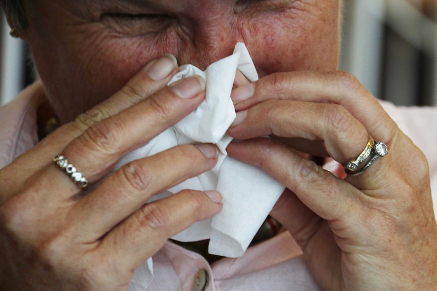 Man holds a tissue to his face to blow his nose.