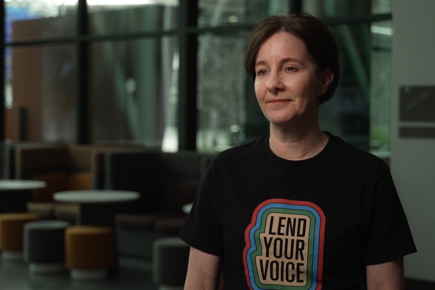 Nadia Rosin, with short dark hair, wears a black T-shirt with the words: Lend your voice.