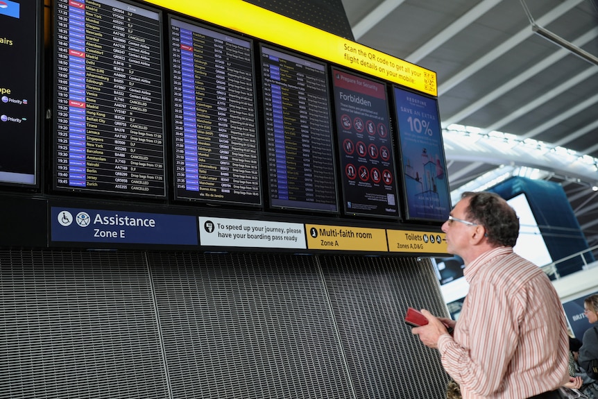 A man looks at an airport screen with cancellation appearing next to many flights