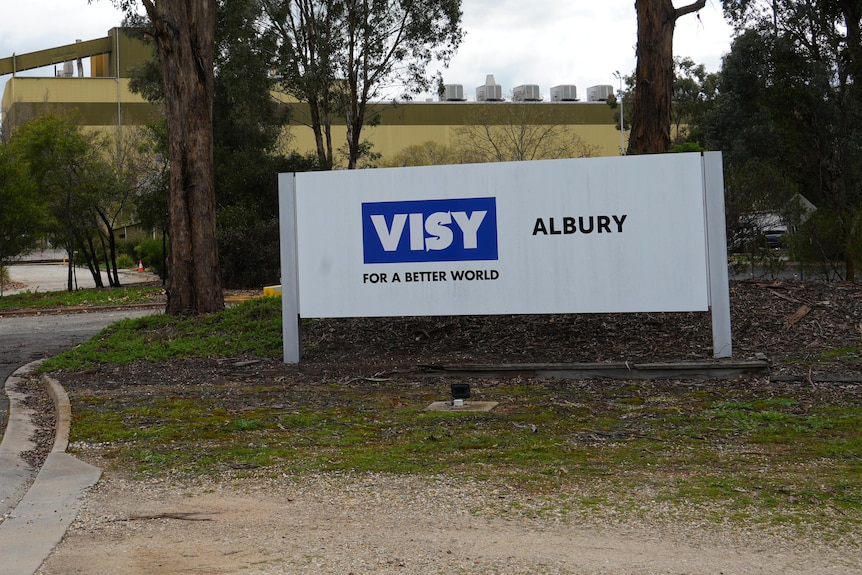A large sign reading "Visy" stands in front of trees and a large industrial-looking building in the background.