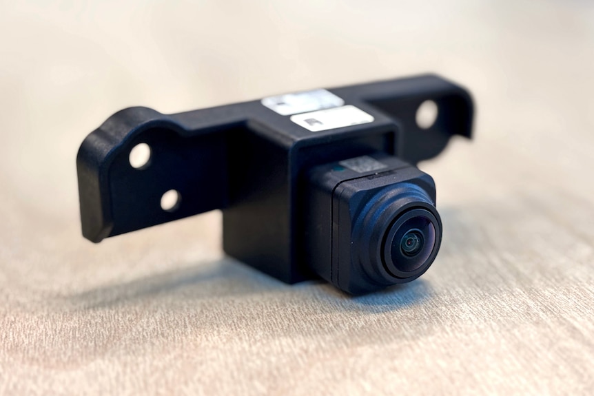 A close-up photo of a small camera lens and the black plastic bracket surrounding it. It is sitting on a table.
