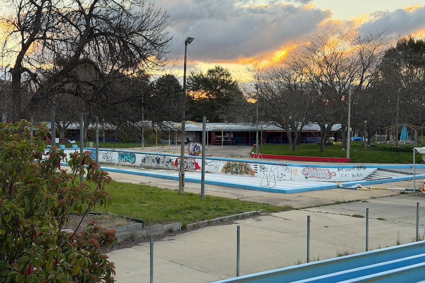 An unused water park pictured at dusk, with an empty swimming pool covered in graffiti.