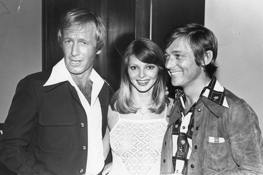 A black and white photo of Paul Hogan, Delvene Delaney and John Cornell all smiling at the camera.