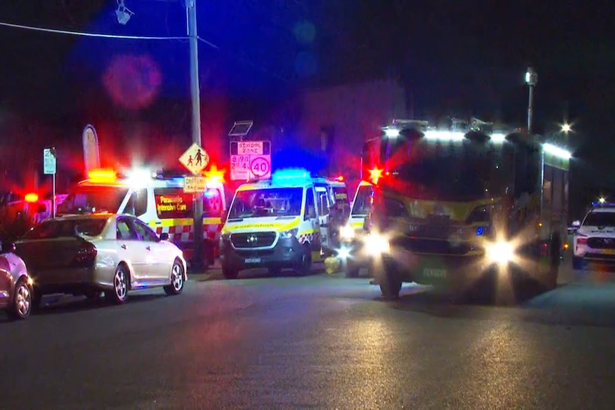 Multiple ambulance and police vehicles on a street with lights at night.