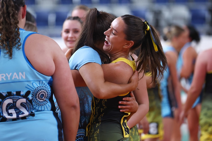 Two netballers from opposing teams hug. One has a large smile